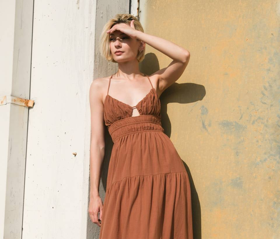 Woman wearing a brown dress standing against a textured wall.